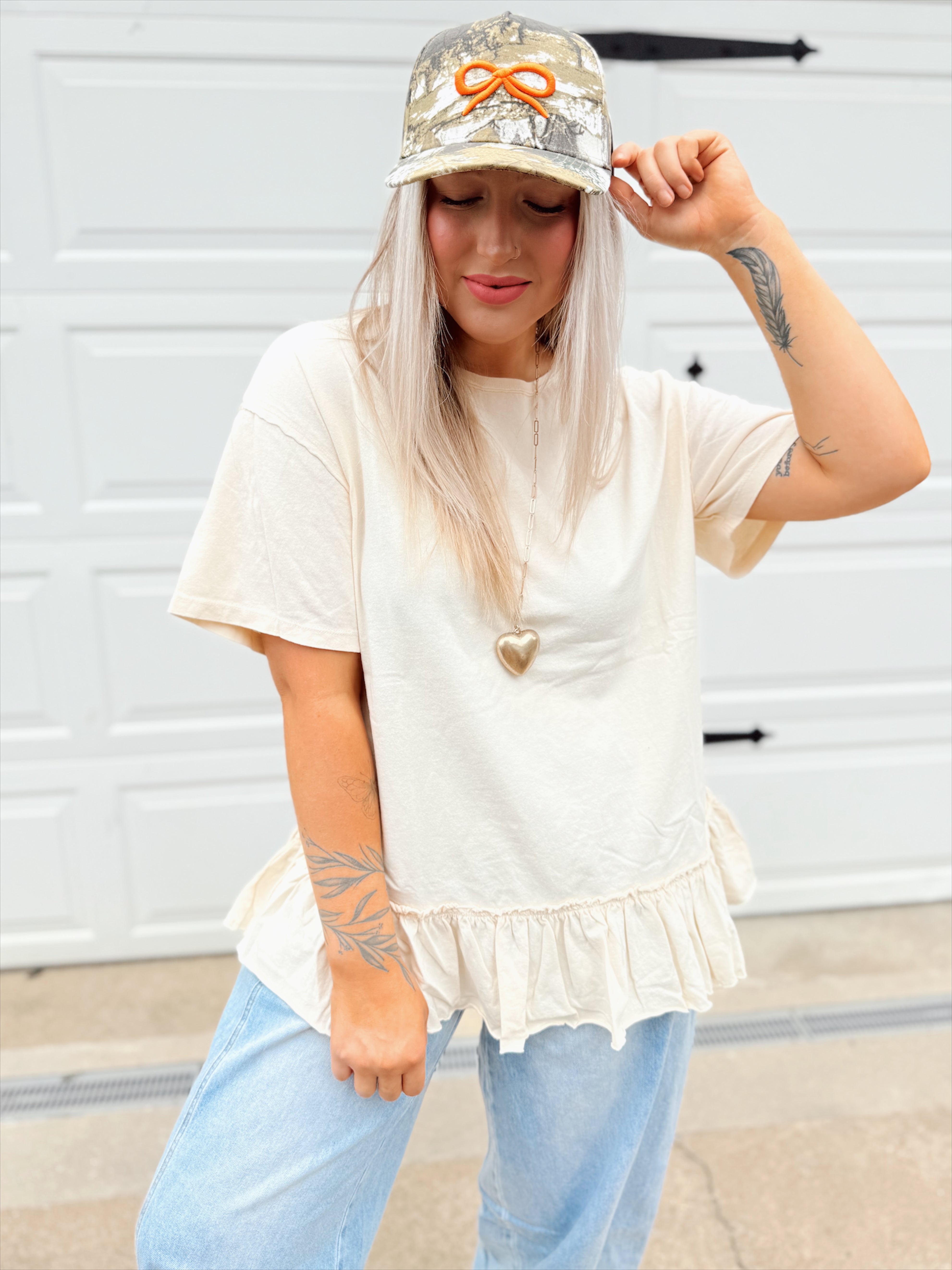 Person wearing a white top with ruffled hem and light blue jeans, standing in front of a white garage door.