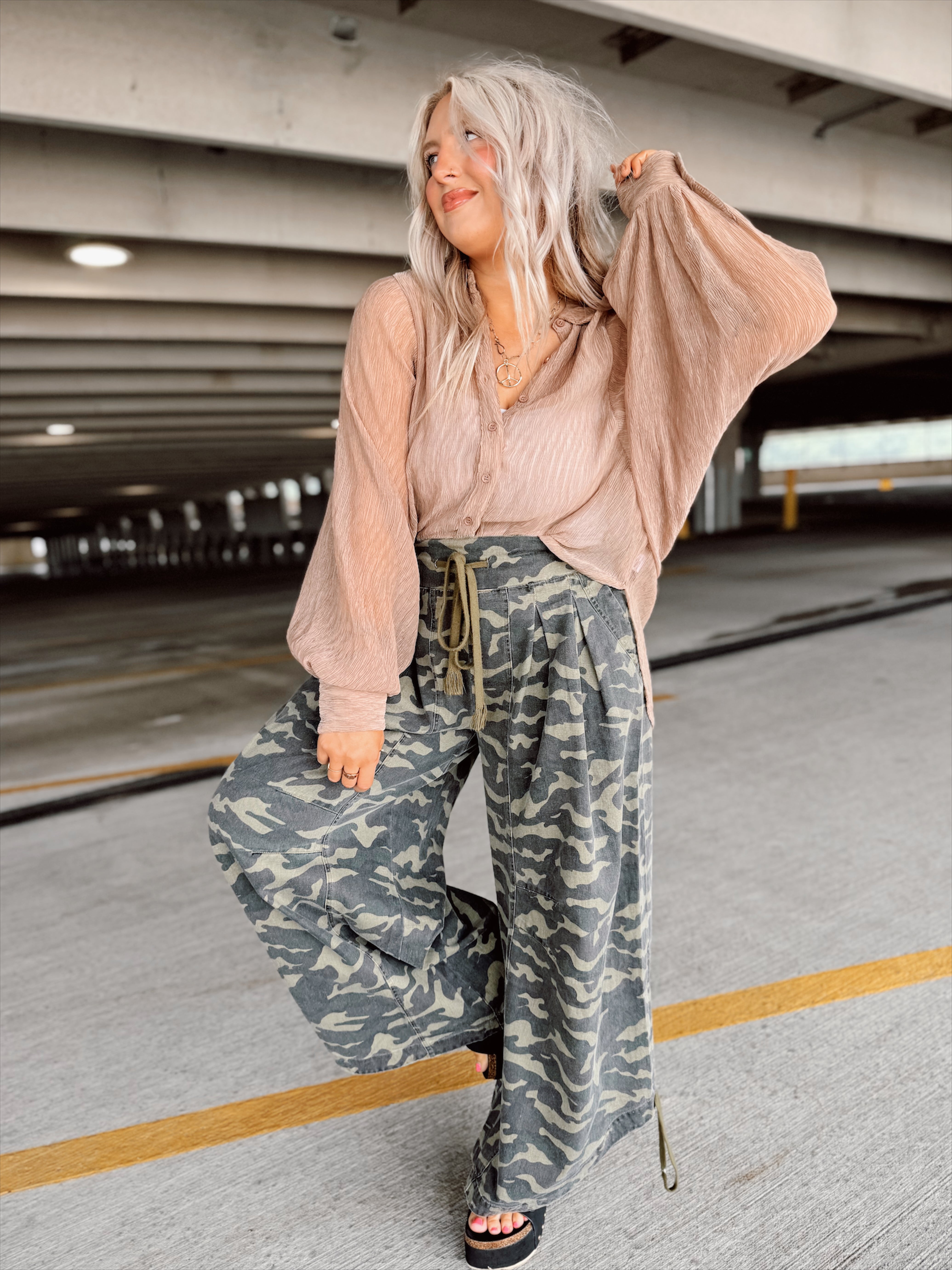 Woman wearing a beige top and camouflage pants in an indoor parking garage.