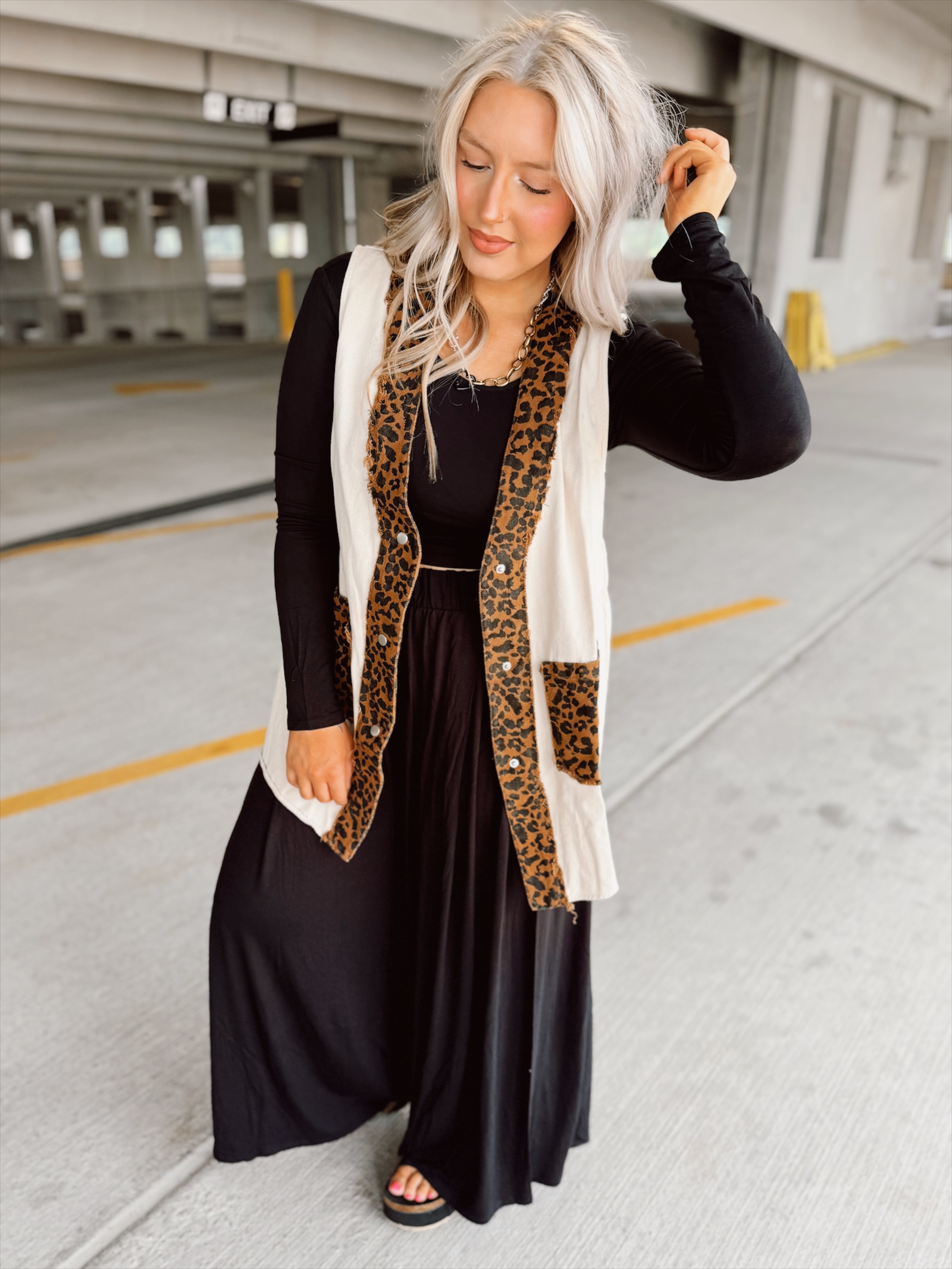 Woman wearing a black outfit with a leopard print vest in an indoor parking garage.