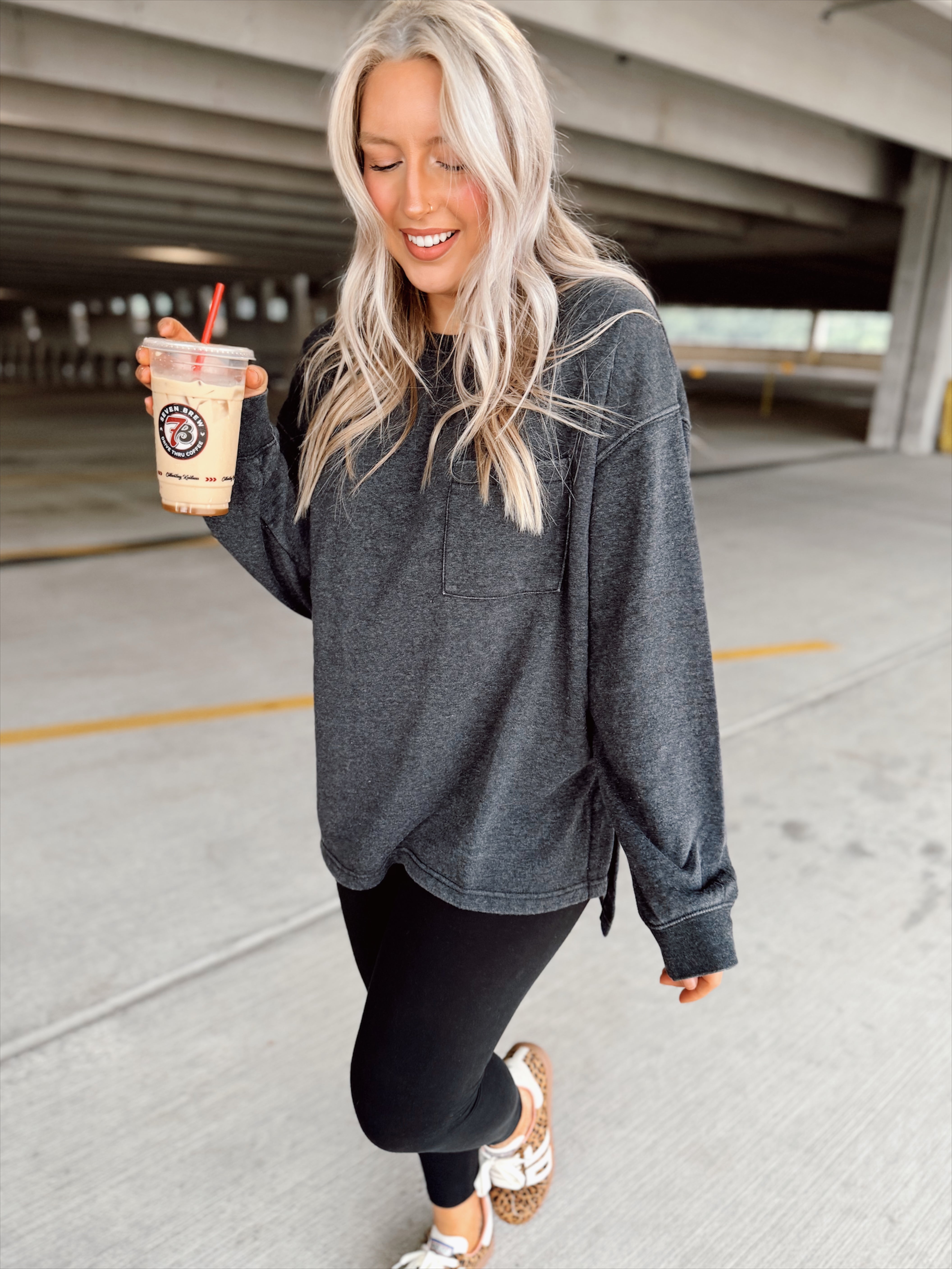Woman in a black sweatshirt and black leggings holding a coffee cup in an indoor parking garage.