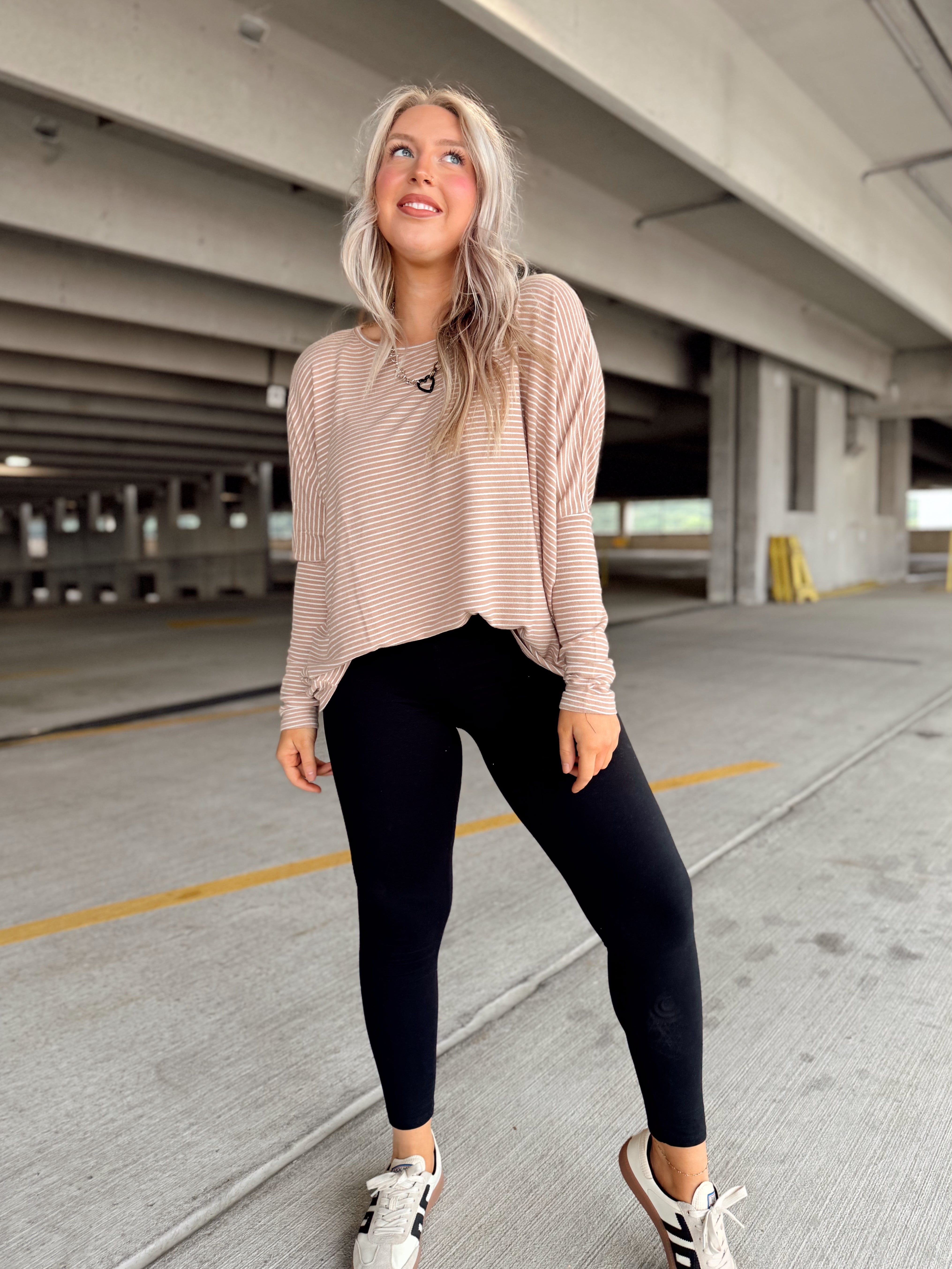 Woman in a beige striped top and black leggings standing in a parking garage.