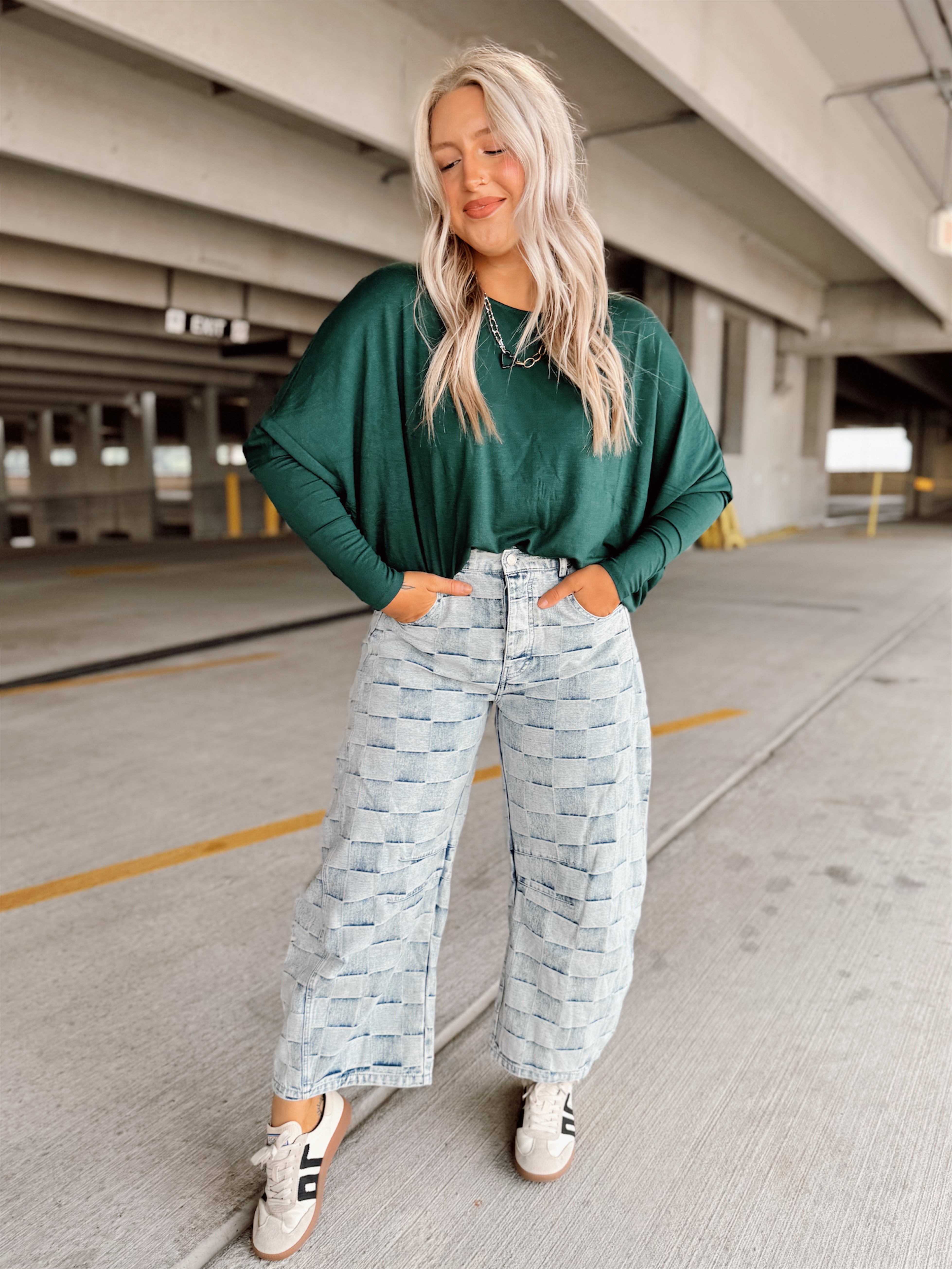 Woman wearing a green sweater and light blue patterned pants standing in a parking garage.