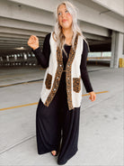 Woman wearing a leopard print vest over a black outfit in an indoor parking garage.
