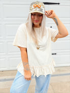 Person wearing a white top with ruffled hem and light blue jeans, standing in front of a white garage door.