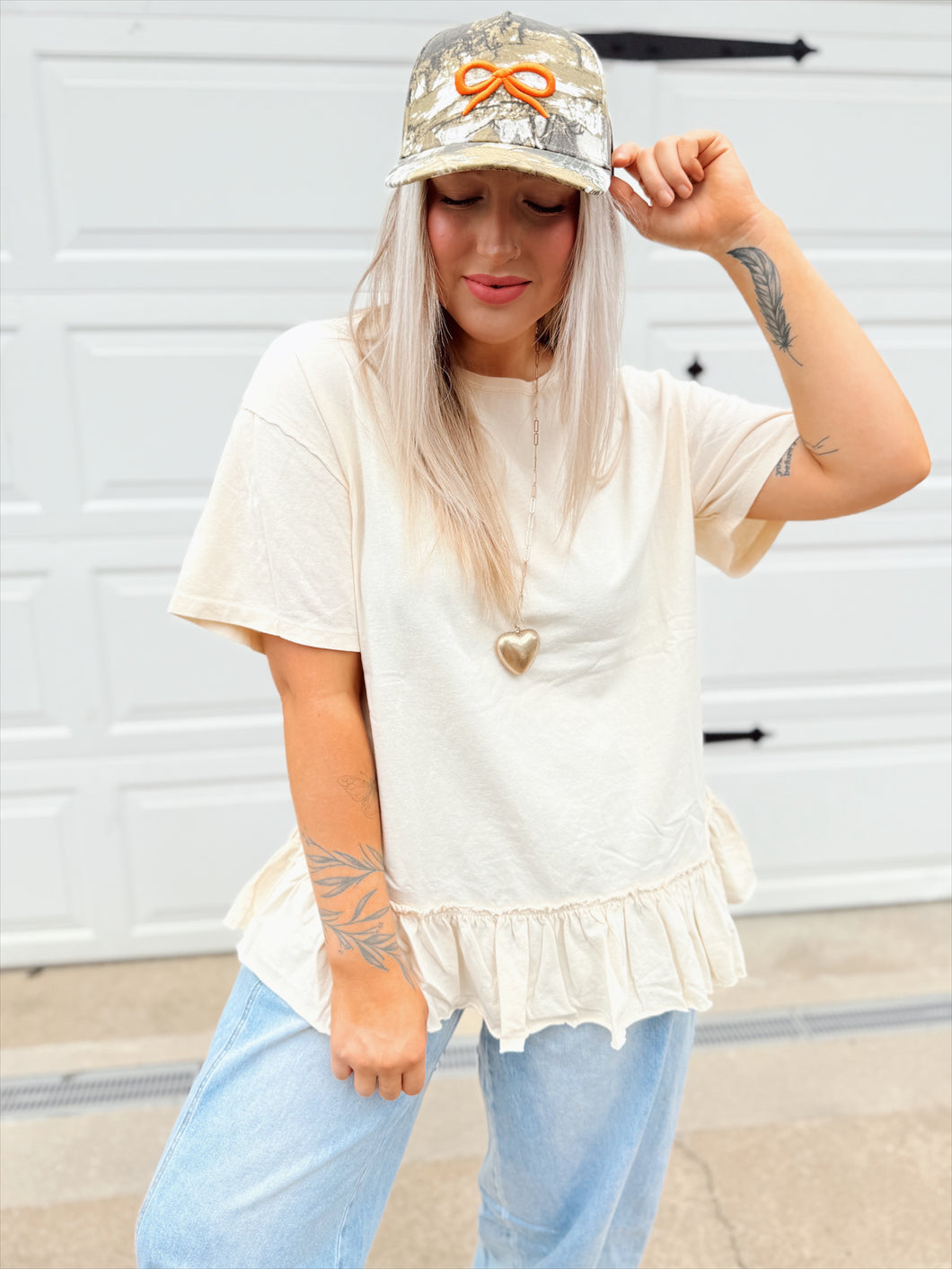 Person wearing a white top with ruffled hem and light blue jeans, standing in front of a white garage door.