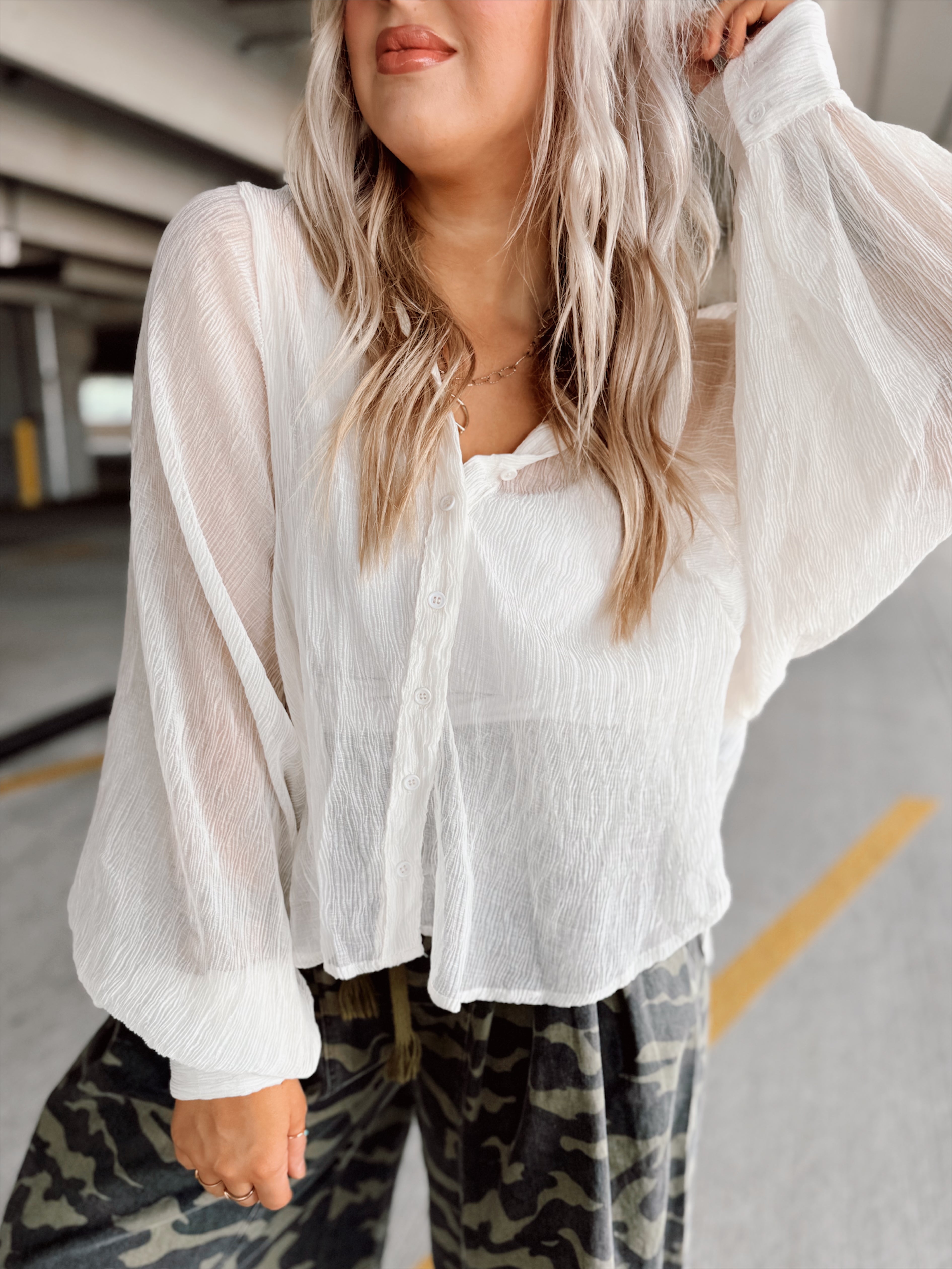 Person wearing a white blouse and camouflage pants in a parking garage.
