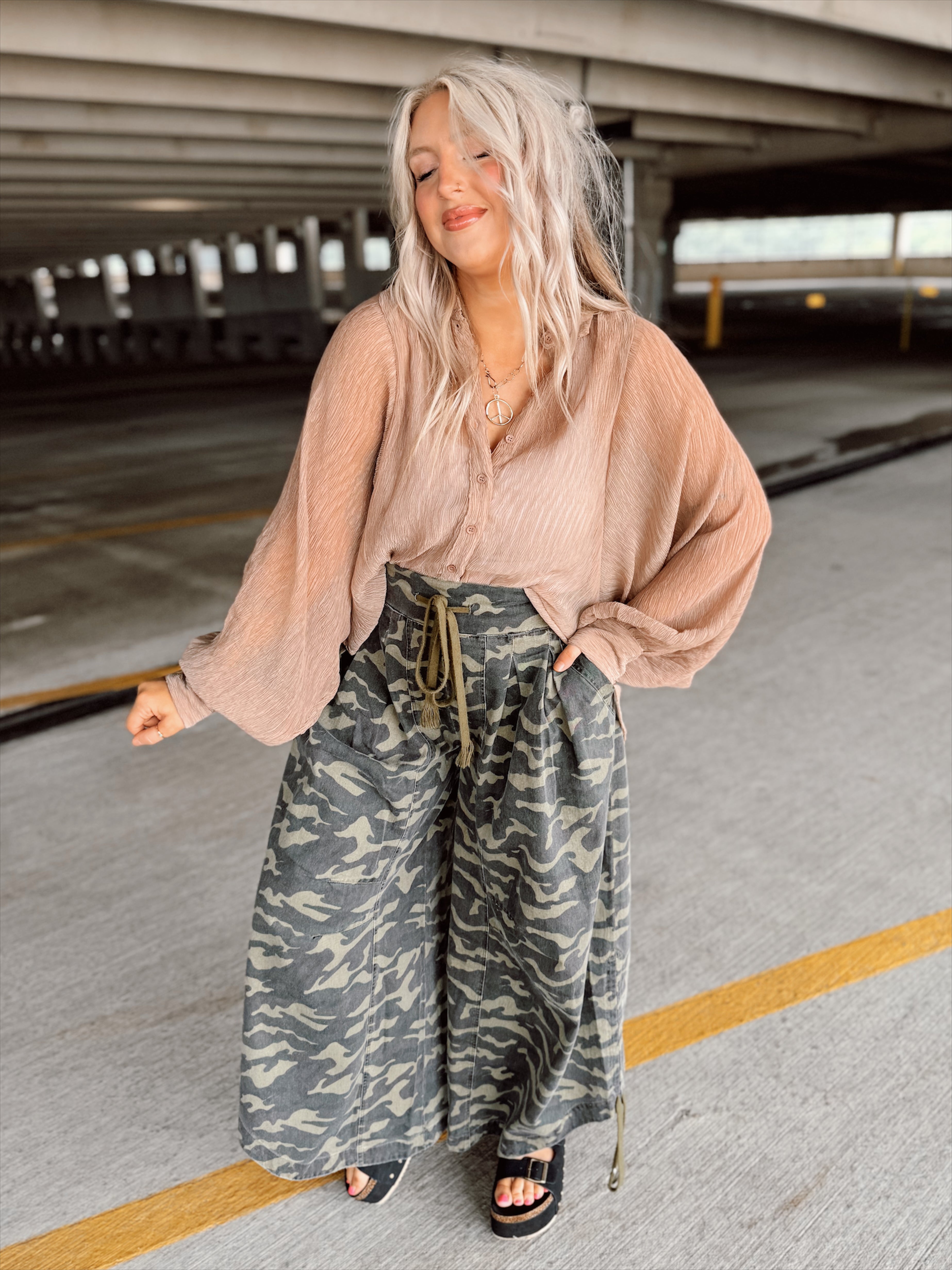 Woman in a brown top and camouflage pants standing in a parking garage