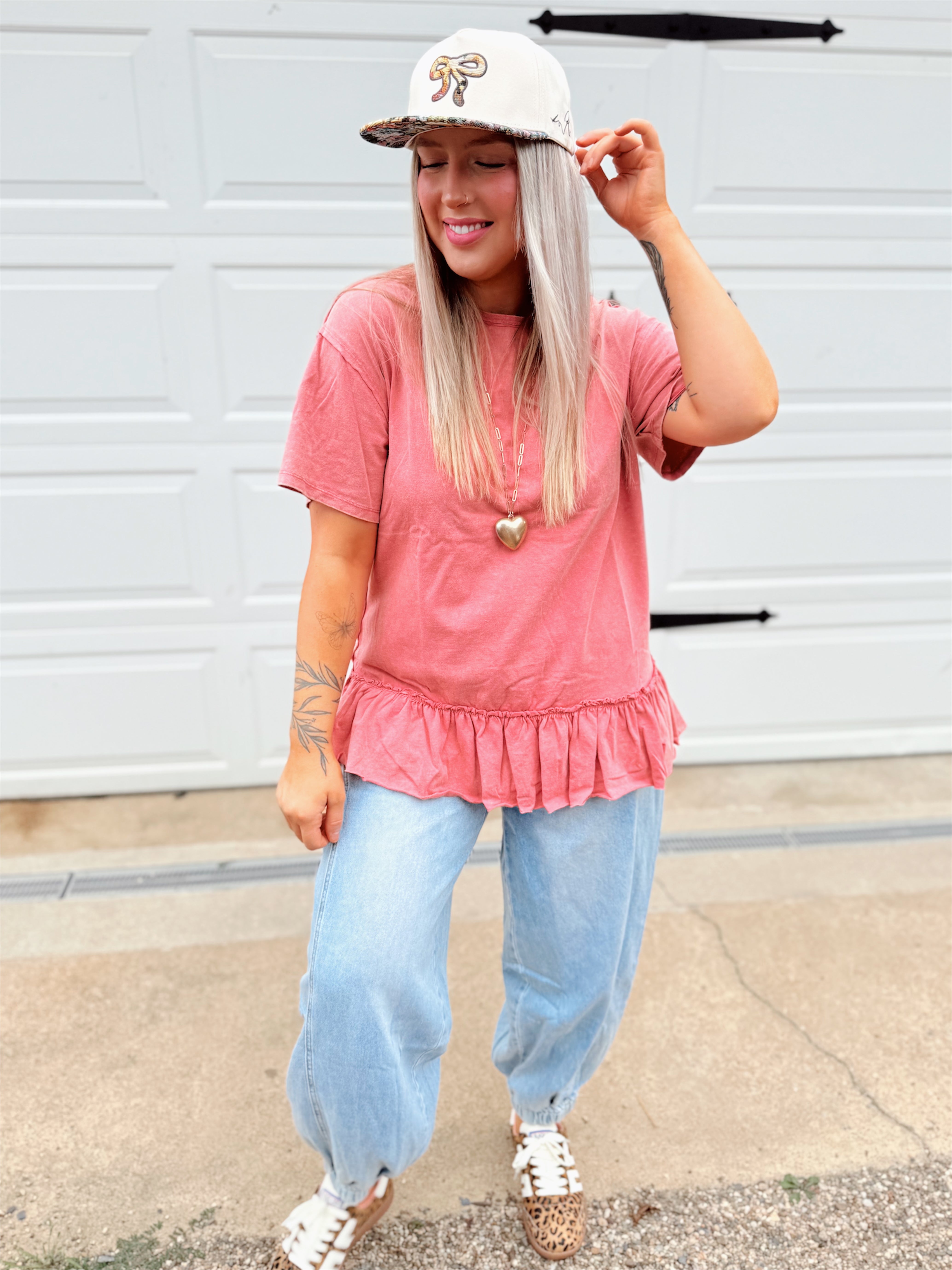 Person wearing a pink peplum top and light blue jeans with a white cap featuring a floral design.