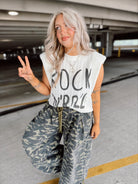 Woman in a parking garage wearing a sleeveless top with text and camouflage pants.