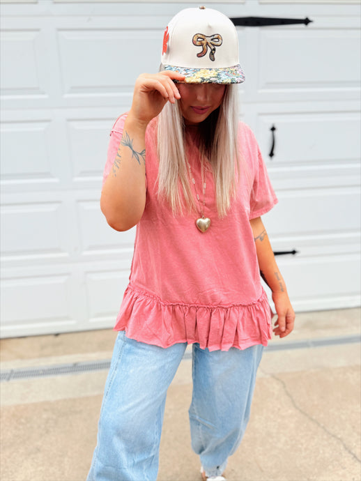 Person wearing a pink peplum top and light blue jeans with a white cap featuring a floral design.