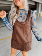 Woman in a brown suede dress with floral top and boots standing in a parking garage.