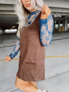 Woman in a brown suede dress with floral top and boots standing in a parking garage.