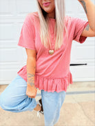 Person wearing a pink peplum top and light blue jeans in front of a garage door.
