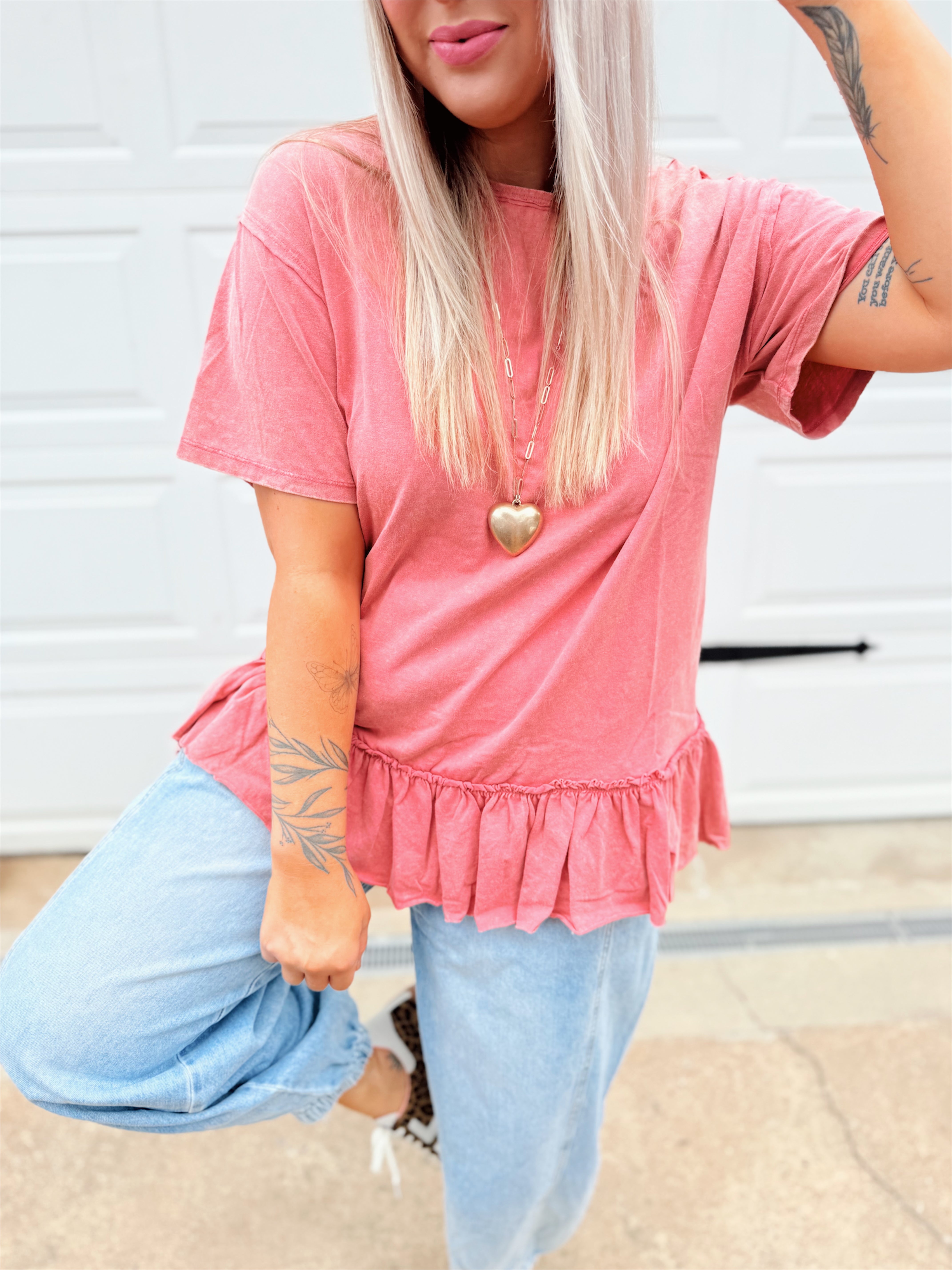 Person wearing a pink peplum top and light blue jeans in front of a garage door.