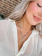 Load image into Gallery viewer, Woman wearing a white shirt with a peace sign necklace, standing against a brick wall.