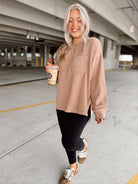 Woman in a beige sweater and black leggings holding a coffee cup in an underground parking lot.