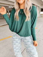 Woman wearing a green sweater and light blue patterned pants standing in a parking garage.