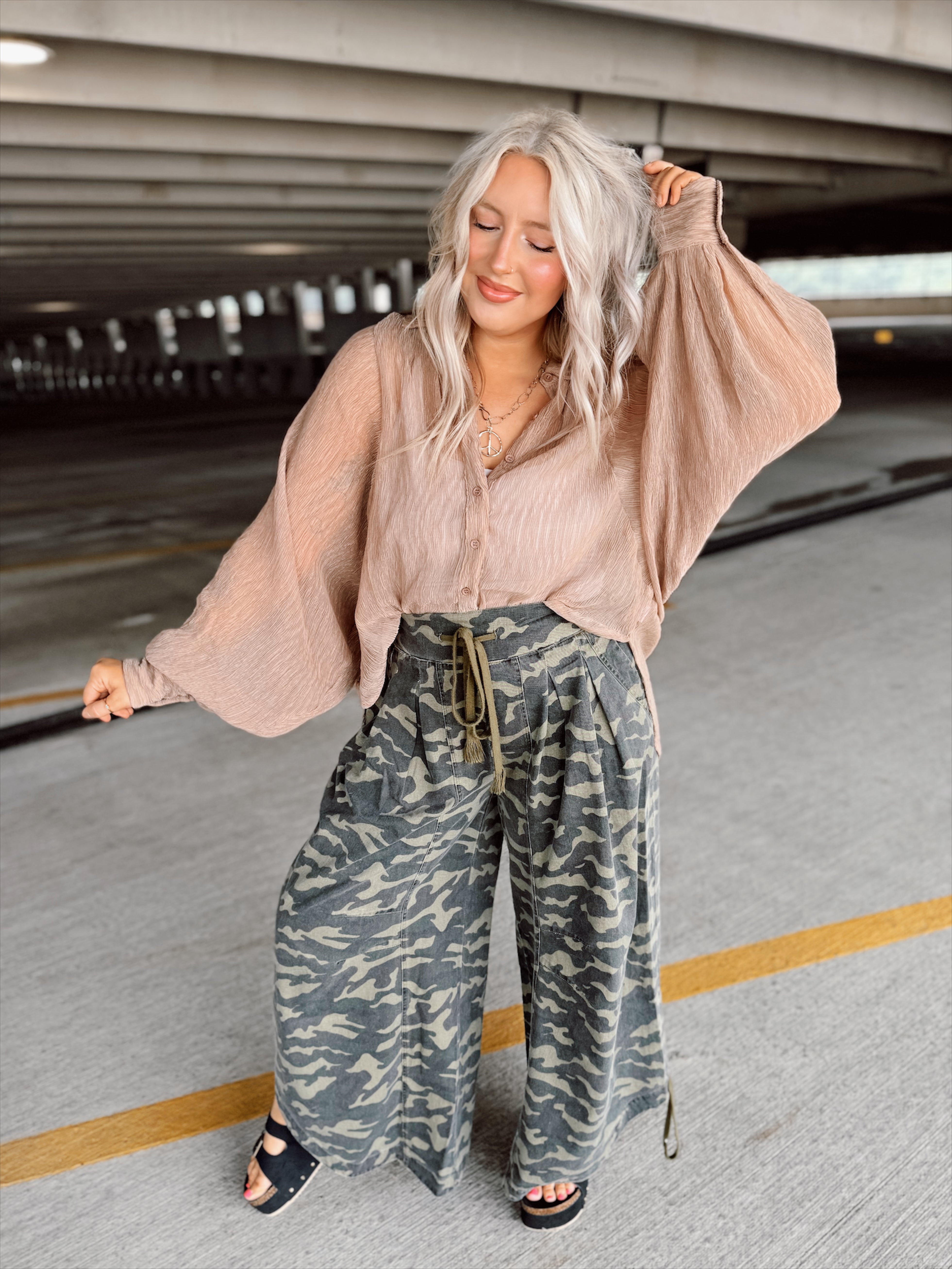 Woman in a brown top and camouflage pants standing in a parking garage
