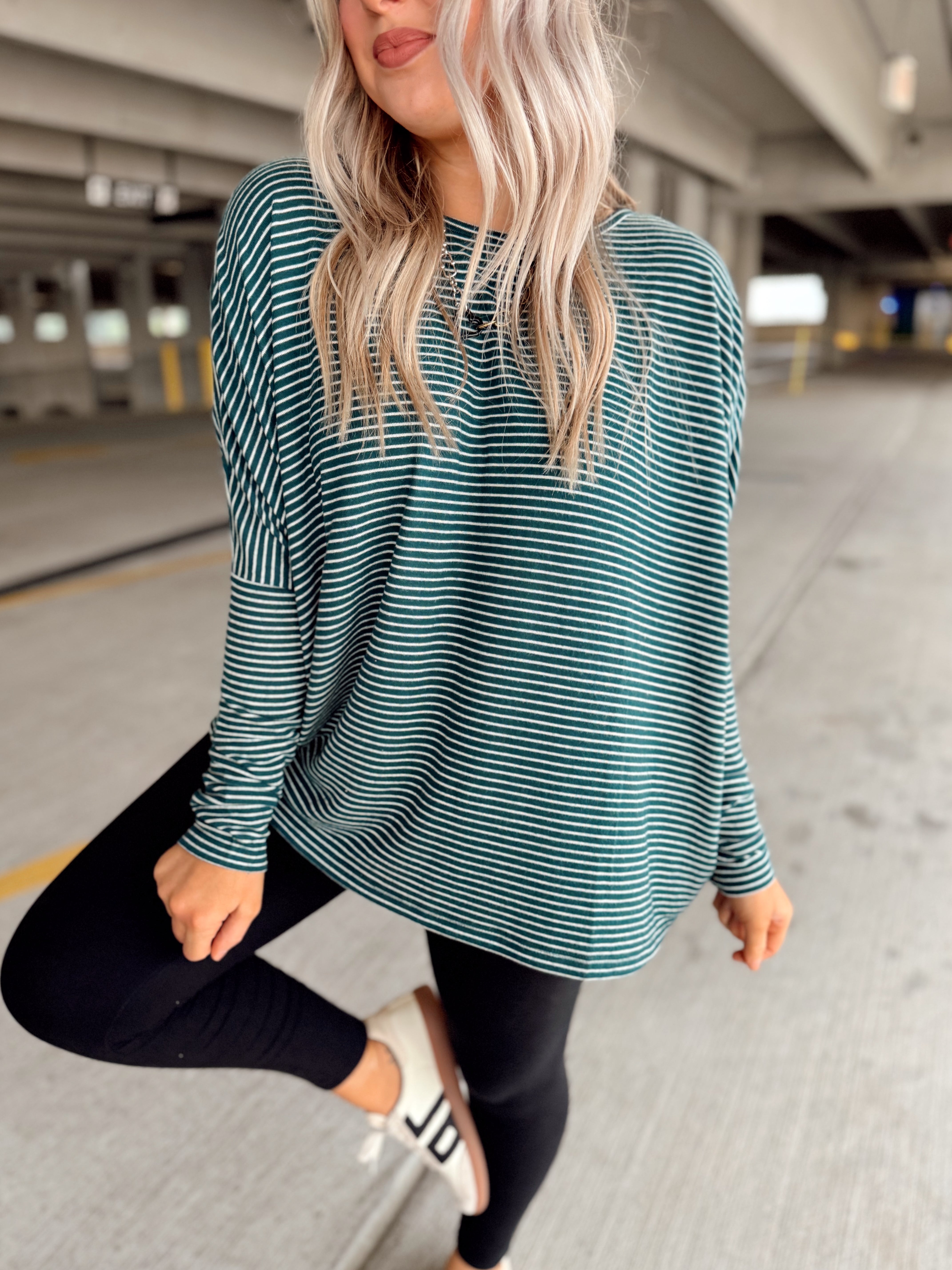 Woman wearing a green and white striped long-sleeve top and black leggings in a parking garage.
