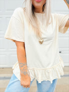 Person wearing a white ruffled t-shirt with a heart-shaped brooch.