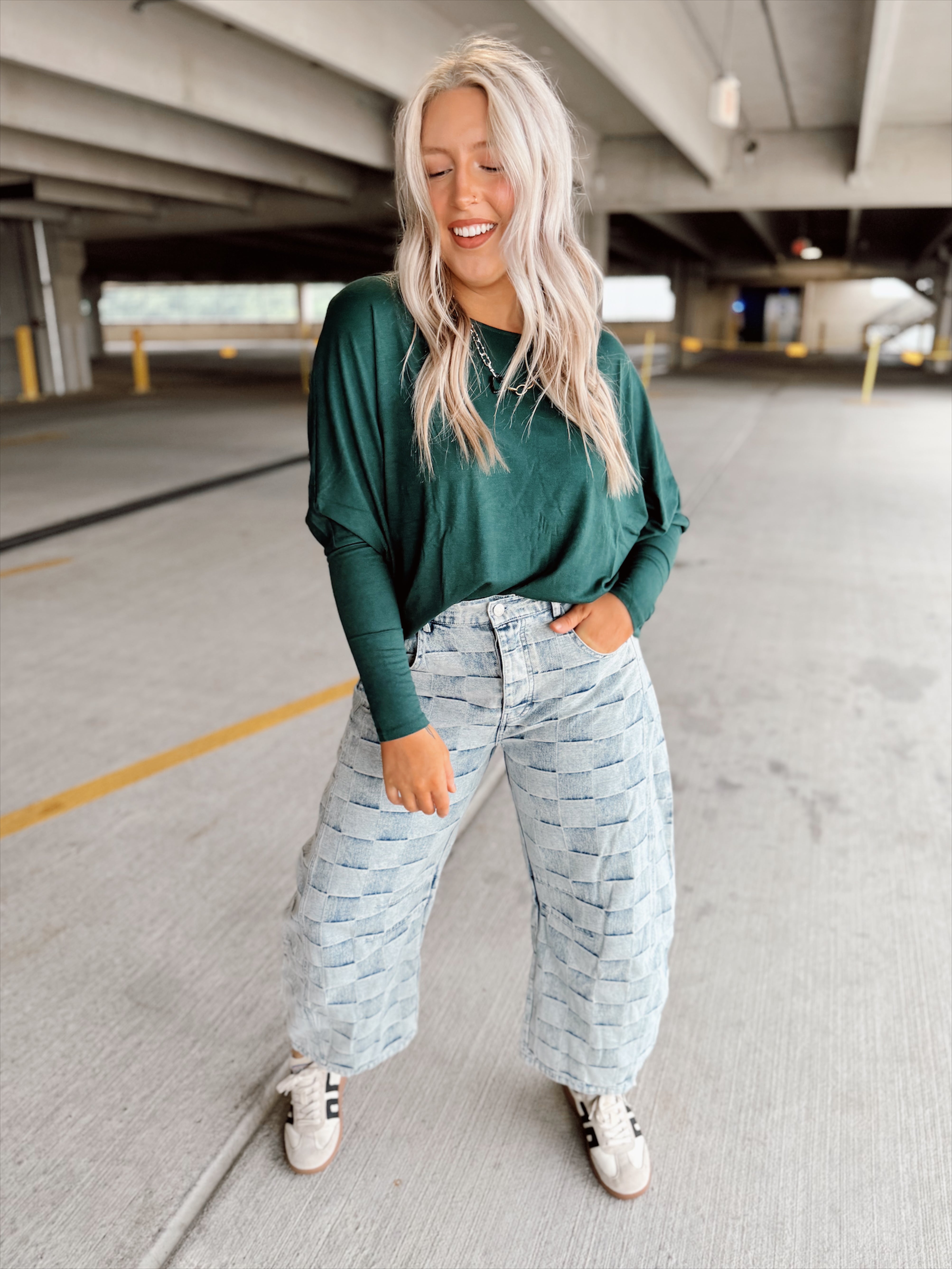 Woman wearing a green sweater and light blue patterned pants standing in a parking garage.