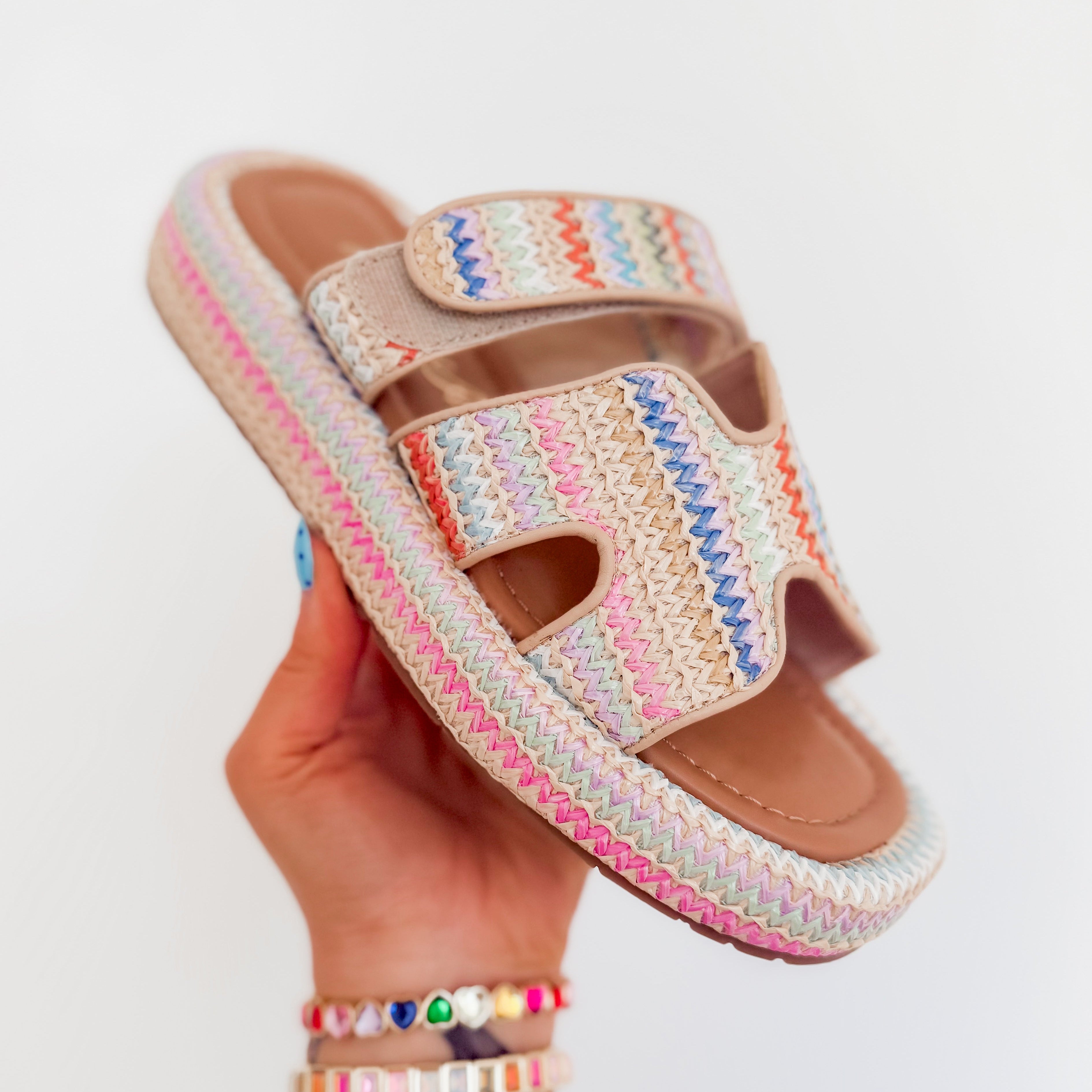 Colorful woven sandal held by a hand with colorful bracelets on a light gray background