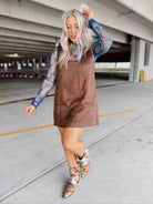 Woman in a brown suede dress with floral top and boots standing in a parking garage.