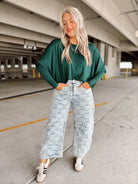 Woman wearing a green sweater and light blue patterned pants standing in a parking garage.