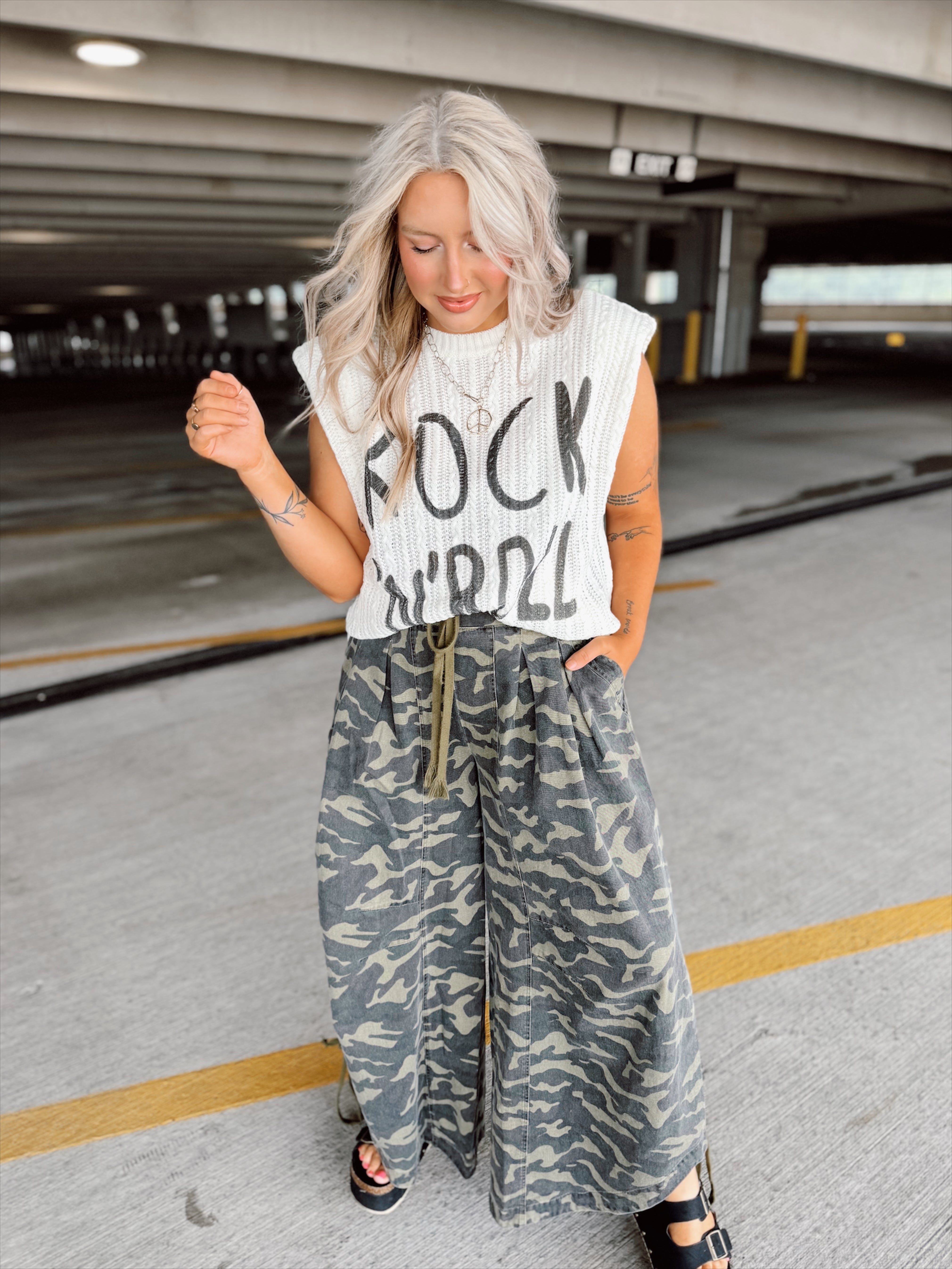 Woman wearing a sleeveless top with 'Rock Roll' text and camouflage pants in an underground parking lot.