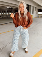 Person wearing a brown long-sleeve top and light blue checkered pants in aparking garage.