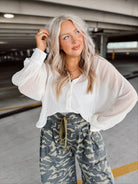 Woman wearing a white blouse and camouflage pants in a parking garage.