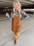 Woman in a brown suede dress with floral top and boots standing in an parking garage.