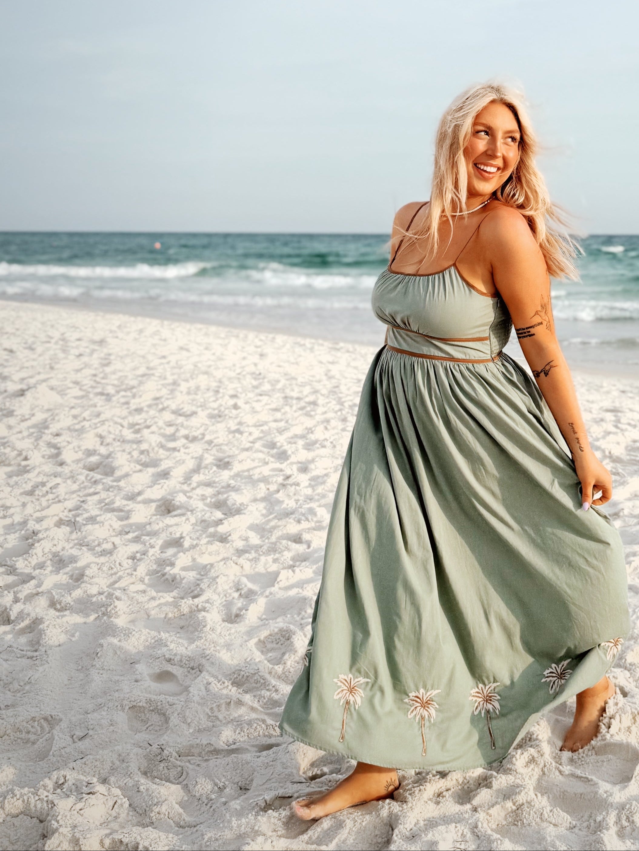 Woman in a green dress standing on a sandy beach with ocean in the background