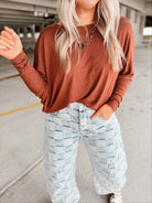 Person wearing a brown long-sleeve top and light blue checkered pants in aparking garage.