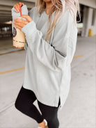 Woman in light sage sweatshirt and black leggings holding a drink in a parking garage.