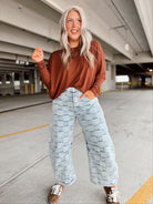 Person wearing a brown long-sleeve top and light blue checkered pants in aparking garage.