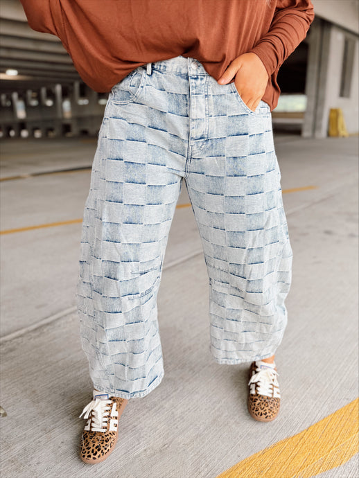 Person wearing a brown top and light blue checkered patterned pants in a parking garage.
