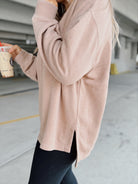 Woman in a beige sweater and black leggings holding a coffee cup in an underground parking lot.