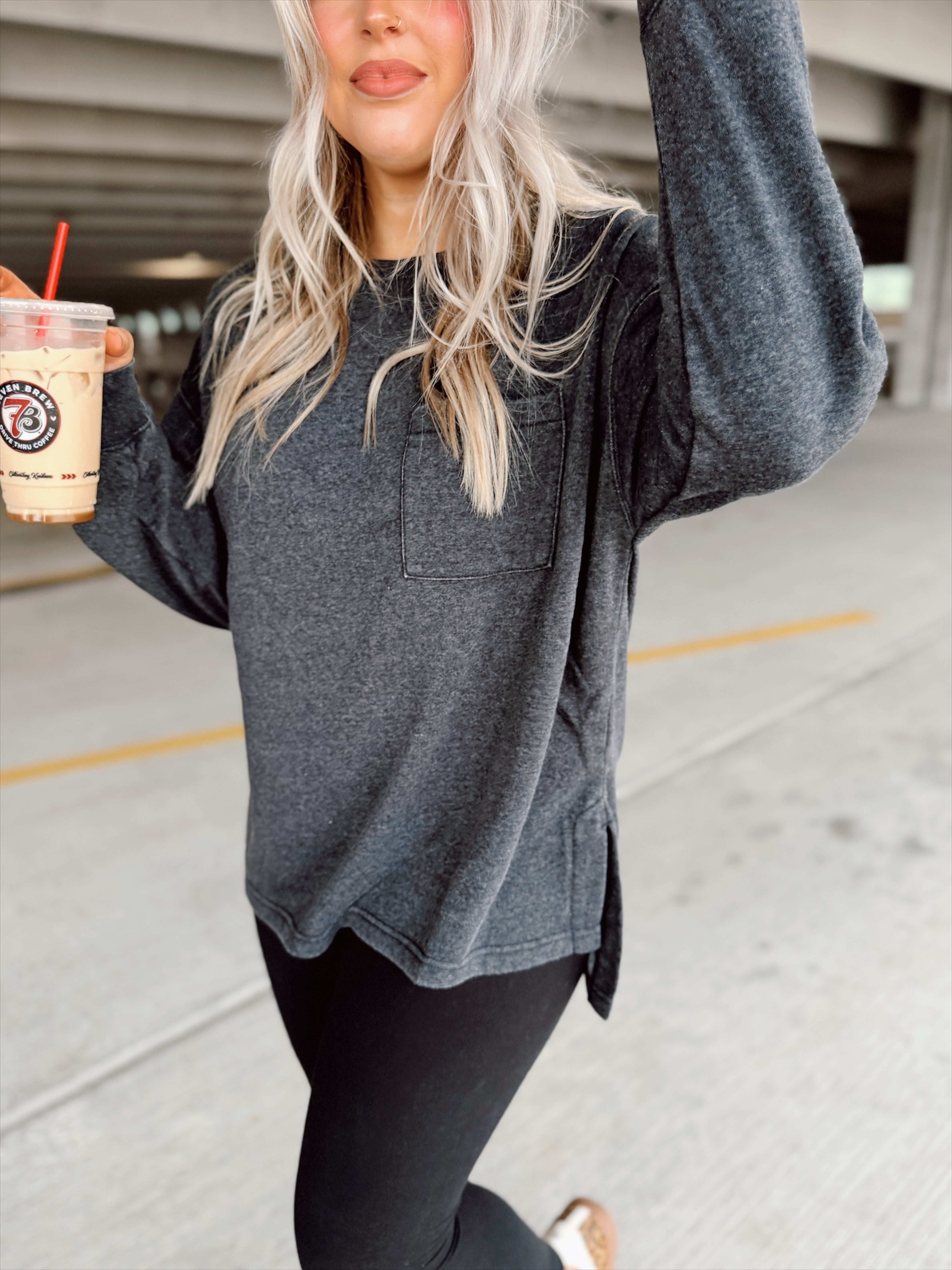 Person wearing a black sweatshirt and black leggings, holding a drink with a straw.