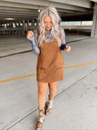 Woman in a brown suede dress with floral top and boots standing in an parking garage.