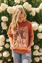 Woman wearing a rust-colored t-shirt with skeleton design in front of white flowers